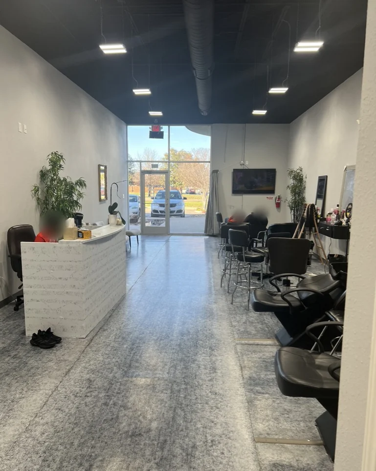 Looking through the salon toward the glass front door: a white marble front desk on the left and styling chairs along the right wall