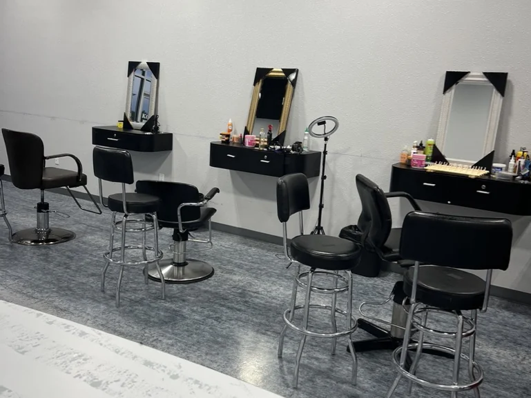 Three styling stations with black mirrors and shelves, salon chairs and stools on a grey floor
